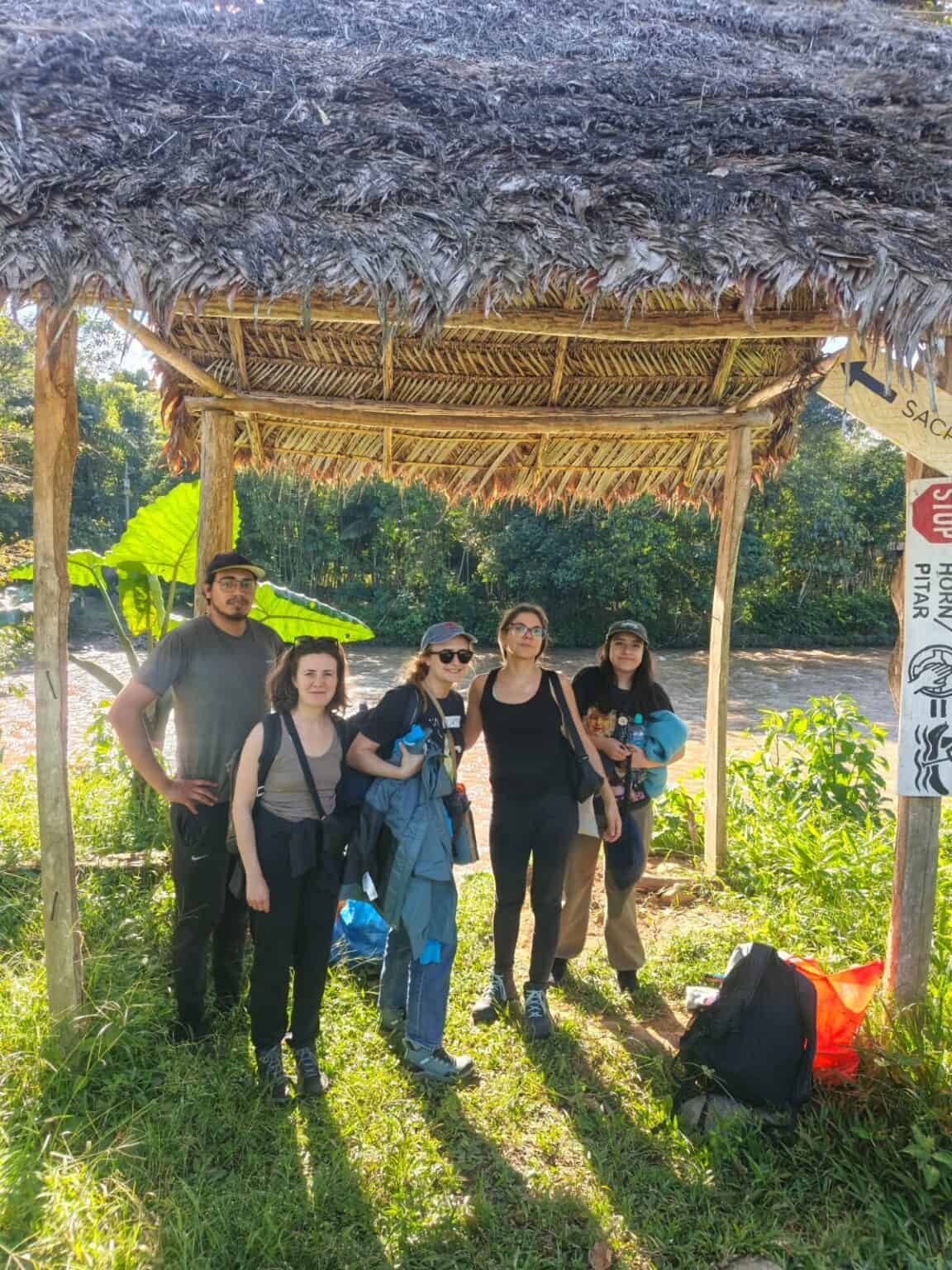 Five hikers under thatched shelter by river