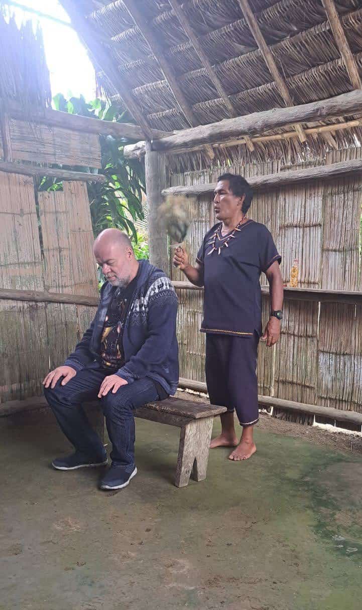 Man fanning seated man inside thatched hut