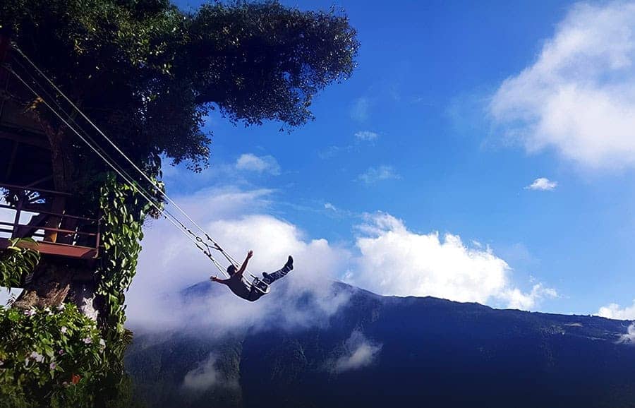 Person swings above misty mountains beneath blue sky